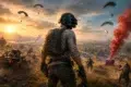 A soldier in tactical gear gazes over a battlefield at sunset. Parachutes descend as a red smoke marker signifies a supply drop. Intense and strategic atmosphere.
