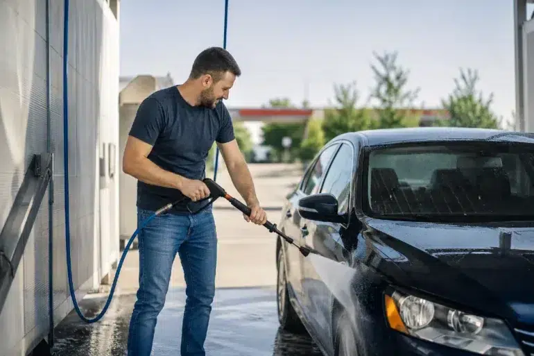 Driver using a self serve car wash near me station to clean a vehicle in a bright local wash bay