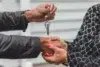 Close-up of a handshake between two people, one holding a house-shaped keychain with a key. The scene conveys trust and a new beginning.