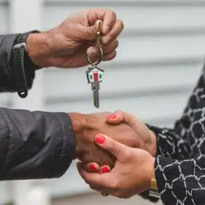 Close-up of a handshake between two people, one holding a house-shaped keychain with a key. The scene conveys trust and a new beginning.