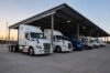 A row of various colored freight trucks parked under a large metal canopy at a professional semi truck storage near me.