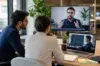 Two hiring professionals conduct a remote evaluation using Technical Interview Outsourcing, appearing on a large monitor and a laptop screen while reviewing a candidate's live coding performance.