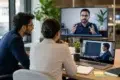 Two hiring professionals conduct a remote evaluation using Technical Interview Outsourcing, appearing on a large monitor and a laptop screen while reviewing a candidate's live coding performance.
