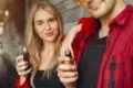 Young woman with long blonde hair smiling while holding a vape device, standing beside a man in a red plaid shirt, creating a relaxed and modern vibe.