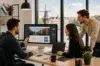 Three colleagues at a web design company in the Netherlands gather around a large desktop monitor and laptops to discuss a website interface design.