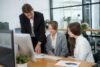 Three business professionals reviewing charts and data at a desk in a modern office setting.