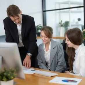 Three business professionals reviewing charts and data at a desk in a modern office setting.