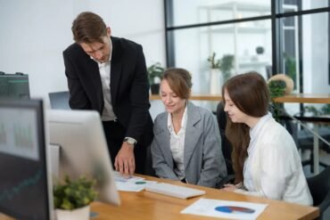 Three business professionals reviewing charts and data at a desk in a modern office setting.