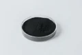 Black powder in a clear round petri dish on a light gray background.