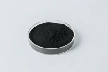 Black powder in a clear round petri dish on a light gray background.