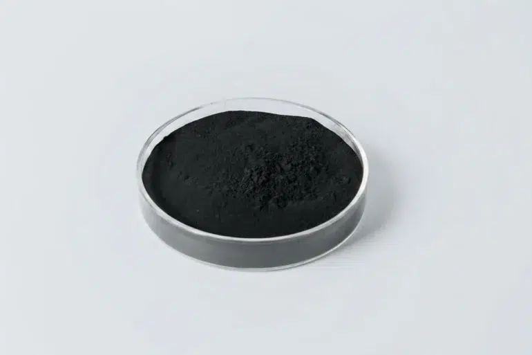 Black powder in a clear round petri dish on a light gray background.