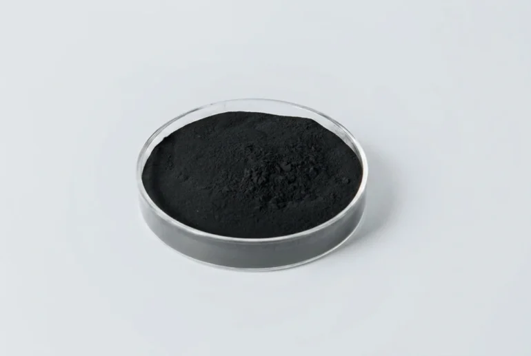 Black powder in a clear round petri dish on a light gray background.