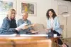 Three professionals discuss documents in a modern office setting with artwork on the wall.