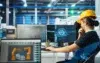 A person in a hard hat and overalls thoughtfully observes computer screens displaying robotic arm designs in a modern industrial setting.