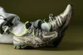 Person wearing gray sweatpants and neon-accented beige athletic shoes, resting feet against a plain olive background.