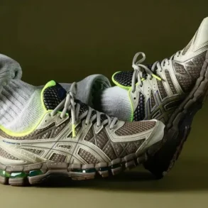 Person wearing gray sweatpants and neon-accented beige athletic shoes, resting feet against a plain olive background.