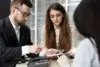 Three professionals in a meeting review documents on a tablet and phone.