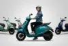 Woman in a helmet riding a teal Chetak electric scooter, with other scooters in various colors behind her.