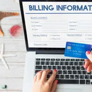 Hands hold a blue credit card over a laptop displaying an online billing form. A starfish and seashells are on the white wooden surface, suggesting a beach theme.