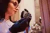 A person wearing black gloves examines a luxury watch under warm lighting. The focus is on the fine details of the watch, suggesting elegance and precision.