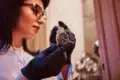 A person wearing black gloves examines a luxury watch under warm lighting. The focus is on the fine details of the watch, suggesting elegance and precision.