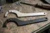 Two adjustable spanner wrenches, one silver and one black, rest on a metal workbench scattered with metal shavings and a worn screwdriver.