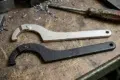 Two adjustable spanner wrenches, one silver and one black, rest on a metal workbench scattered with metal shavings and a worn screwdriver.
