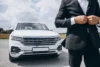 White luxury SUV parked outdoors with a man in a black suit buttoning his jacket in the foreground.