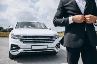 White luxury SUV parked outdoors with a man in a black suit buttoning his jacket in the foreground.