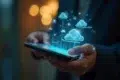 A person holds a smartphone with glowing blue 3D cloud icons hovering above it, symbolizing cloud technology. The background is softly blurred, creating a futuristic and innovative feel.