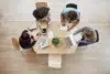 Overhead view of four people collaborating around a light wood table with laptops, tablets, and notebooks.