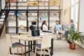 Three people converse in a modern office with bookshelves and collaborative workspaces.