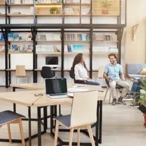 Three people converse in a modern office with bookshelves and collaborative workspaces.
