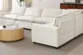 Modern white sectional sofa with plush cushions in a bright living room, featuring a round wooden coffee table on a beige rug.