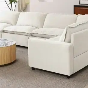 Modern white sectional sofa with plush cushions in a bright living room, featuring a round wooden coffee table on a beige rug.