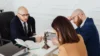 Lawyer in glasses consults with a couple at a desk with a statue of Lady Justice.
