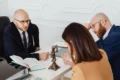 Lawyer in glasses consults with a couple at a desk with a statue of Lady Justice.