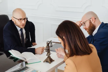Lawyer in glasses consults with a couple at a desk with a statue of Lady Justice.