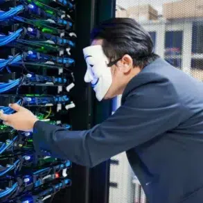 A person in a suit wearing a Guy Fawkes mask interacts with servers in a server room. Blue cables and glowing lights create a mysterious atmosphere.