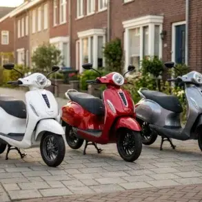 Three scooters in white, red, and silver are parked on a residential street with brick houses and greenery in the background, creating a serene urban scene.