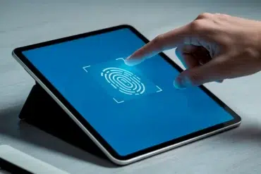 A hand touches a tablet screen displaying a large fingerprint icon on a blue background, symbolizing biometric security. The setting is minimal and modern.