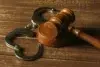 Metal handcuffs rest on a wooden surface next to a wooden gavel.