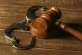 Metal handcuffs rest on a wooden surface next to a wooden gavel.