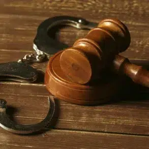 Metal handcuffs rest on a wooden surface next to a wooden gavel.