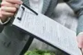A person holding a clipboard with documents, showcasing a professional setting and paperwork for review or signing.