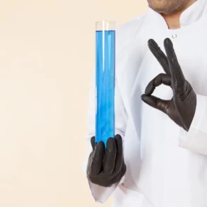 A scientist in a white coat and black gloves holds a large test tube filled with blue liquid, making an "OK" gesture. The tone is professional and precise.