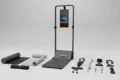 Foldable treadmill with built-in screen, accompanied by various fitness accessories and mats arranged on a plain surface.