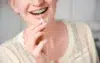 A person smiles while using an interdental brush to clean their braces. The background is soft and neutral, emphasizing dental hygiene and care.