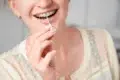 A person smiles while using an interdental brush to clean their braces. The background is soft and neutral, emphasizing dental hygiene and care.