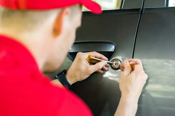 A person in a red uniform skillfully picks a car lock using professional tools. The image conveys a sense of focus and expertise in locksmithing.